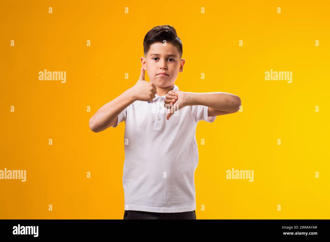 Portrait of kid boy showing thumb up and thumb down gesture over yellow ...
