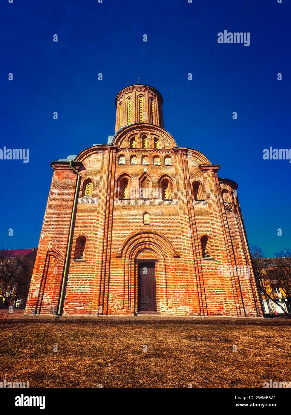 A red brick church with a cylindrical tower, arched doorways, and circular windows under a clear blue sky. Friday Church in Chernihiv. Stock Photo