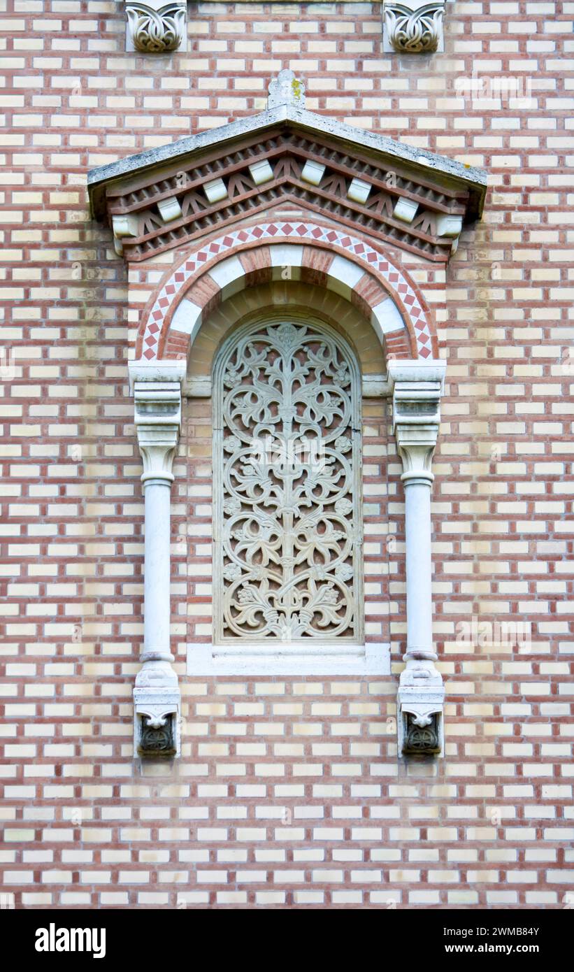 Stone lattice window with intricate tracery, framed by elegant white columns and set within a context of carefully arranged red bricks, adorned with o Stock Photo