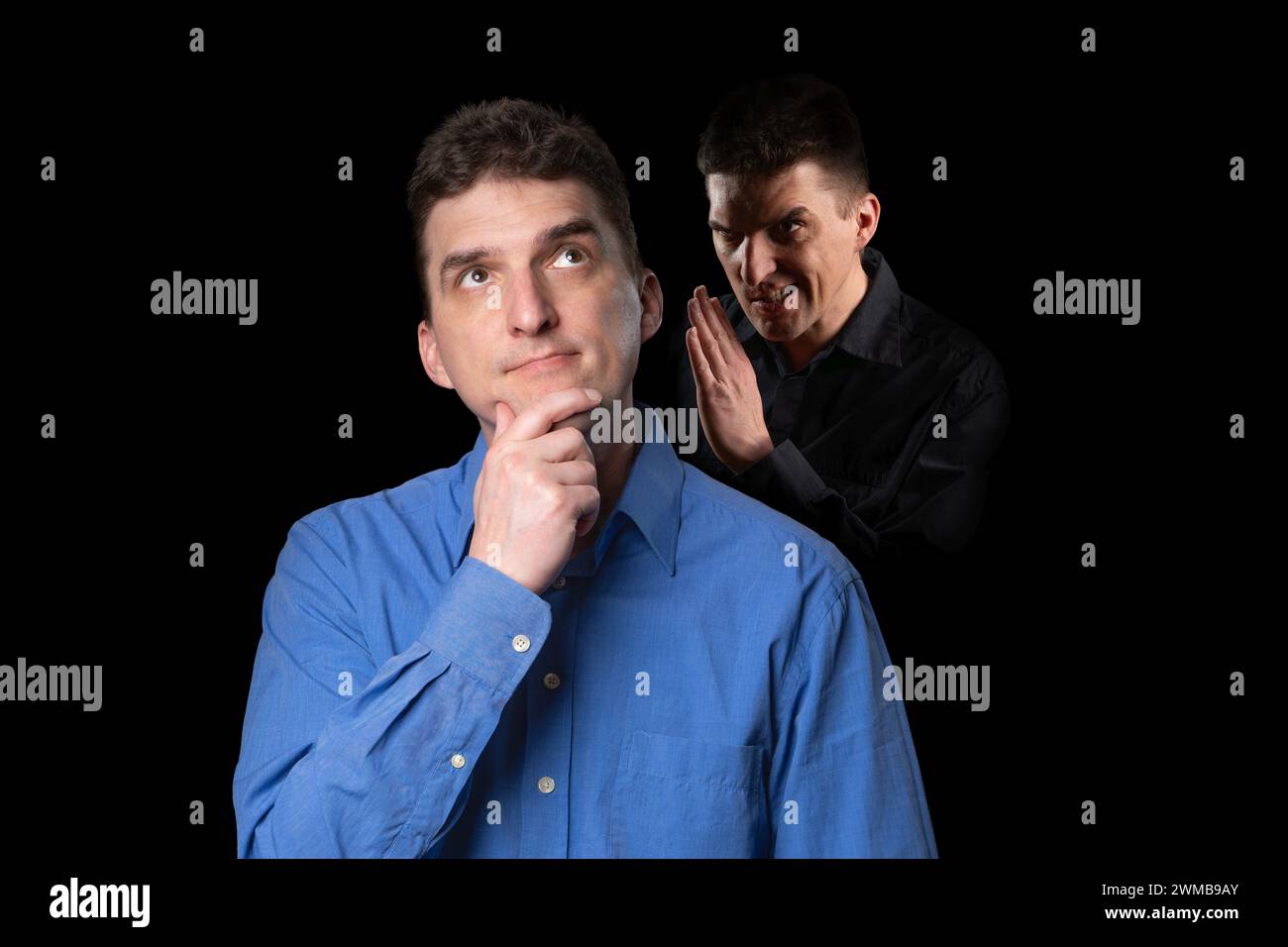 A friendly-looking young man to whom his evil inner voice is whispering something from the shadow behind Stock Photo