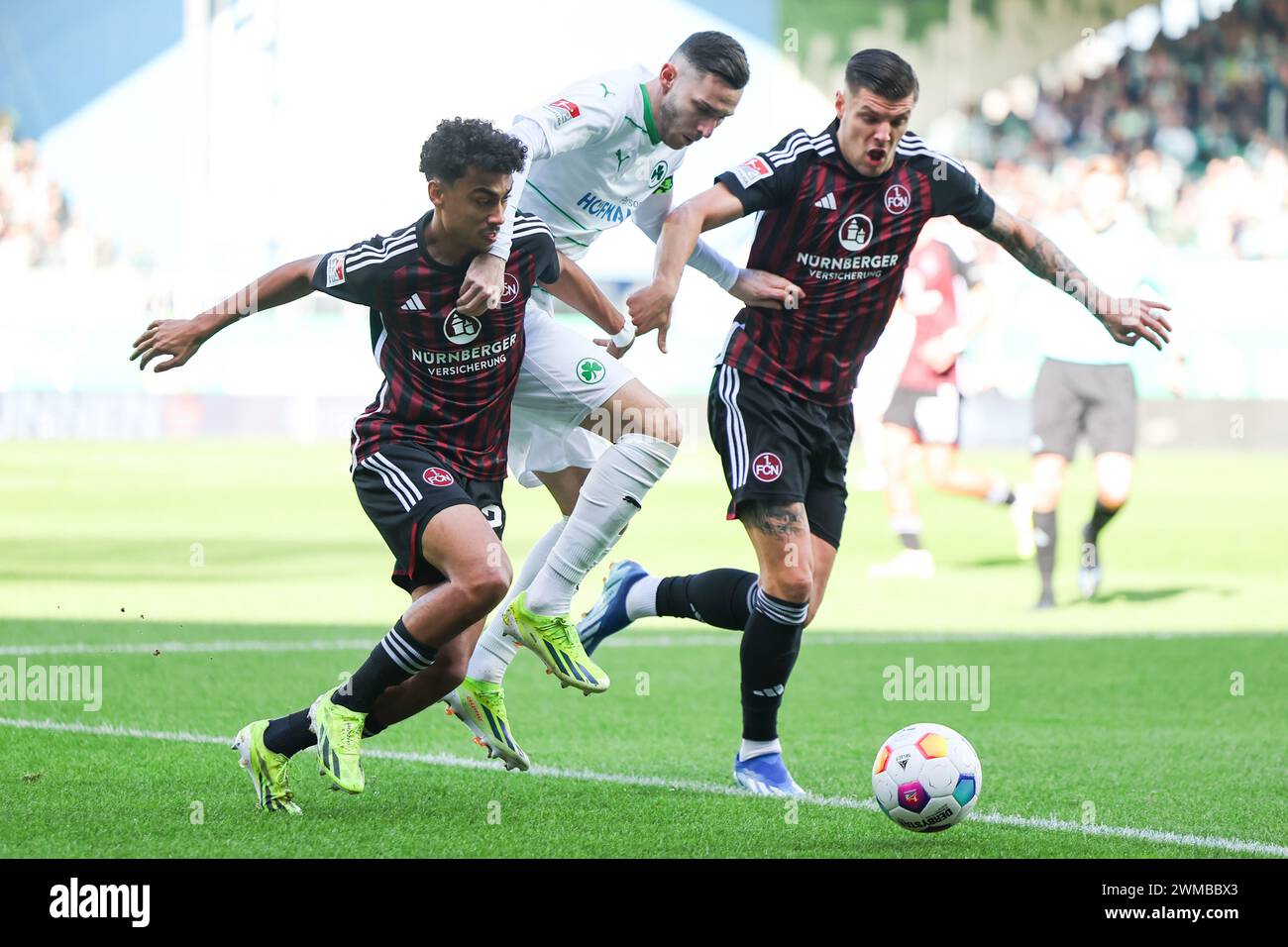 25 February 2024, Bavaria, Fürth: Soccer: Bundesliga 2, SpVgg Greuther Fürth - 1. FC Nürnberg, Matchday 23 at Sportpark Ronhof Thomas Sommer. Fürth's Branimir Hrgota (center) battles for the ball with Nuremberg's Nathaniel Brown (left) and Erik Wekesser. Photo: Daniel Karmann/dpa - IMPORTANT NOTE: In accordance with the regulations of the DFL German Football League and the DFB German Football Association, it is prohibited to utilize or have utilized photographs taken in the stadium and/or of the match in the form of sequential images and/or video-like photo series. Stock Photo