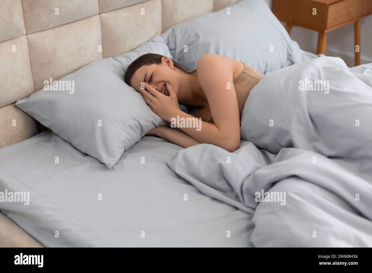 Depressed woman in bed, laughing to mask sadness, feeling isolated Stock Photo