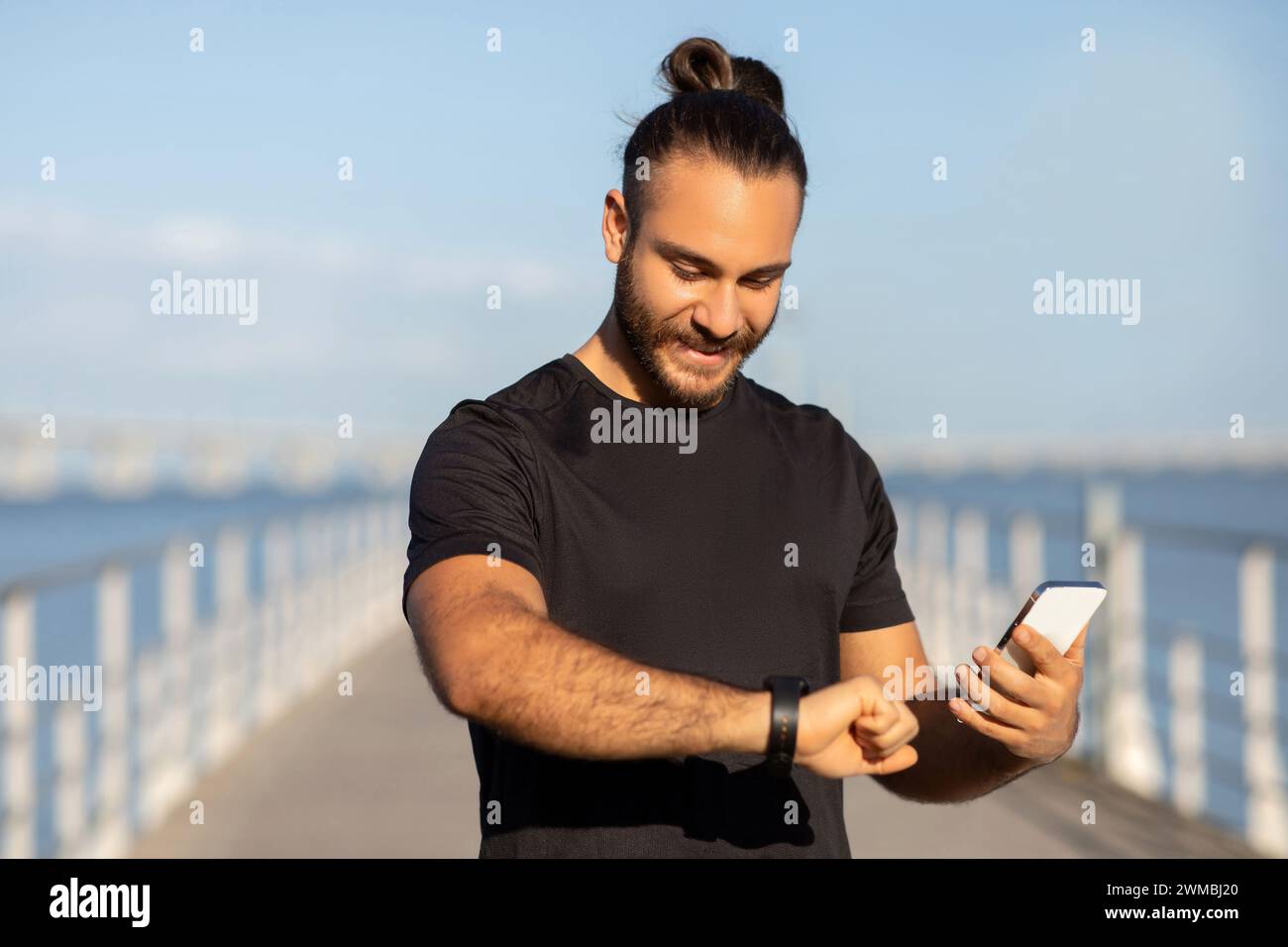 sporty guy checking pulse on fitness tracker holding smartphone outdoor Stock Photo