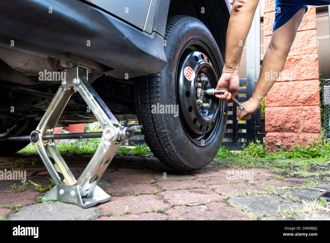 Person attempting to tighten nuts onto temporary car wheel after