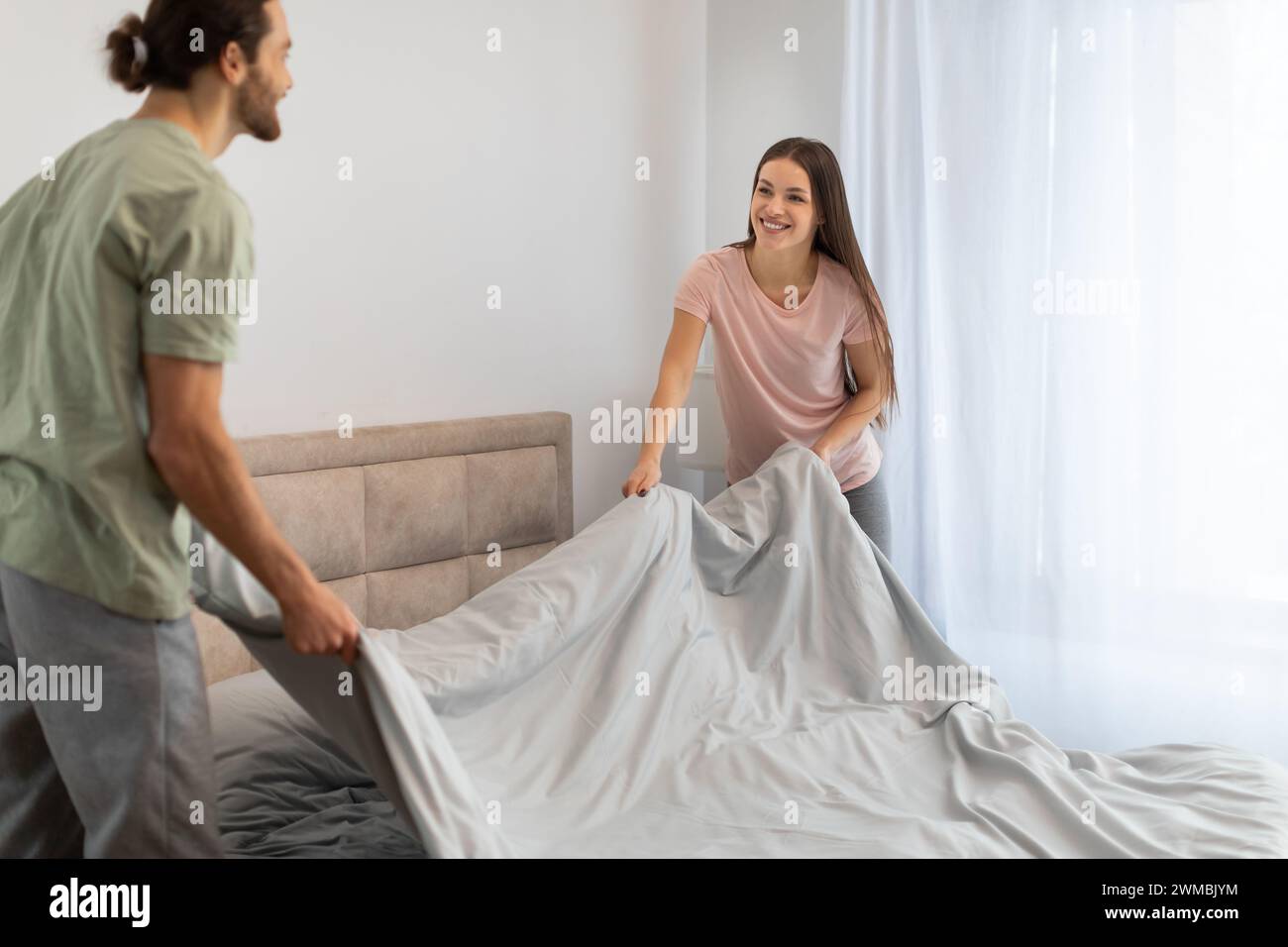 Happy young couple making bed together, teamwork Stock Photo