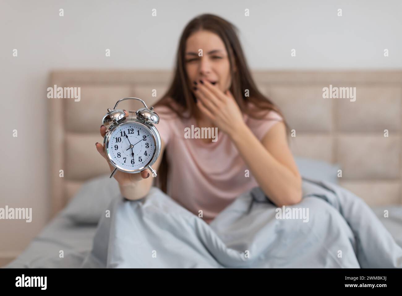 Tired woman in bed with alarm clock, yawning early in the morning Stock Photo