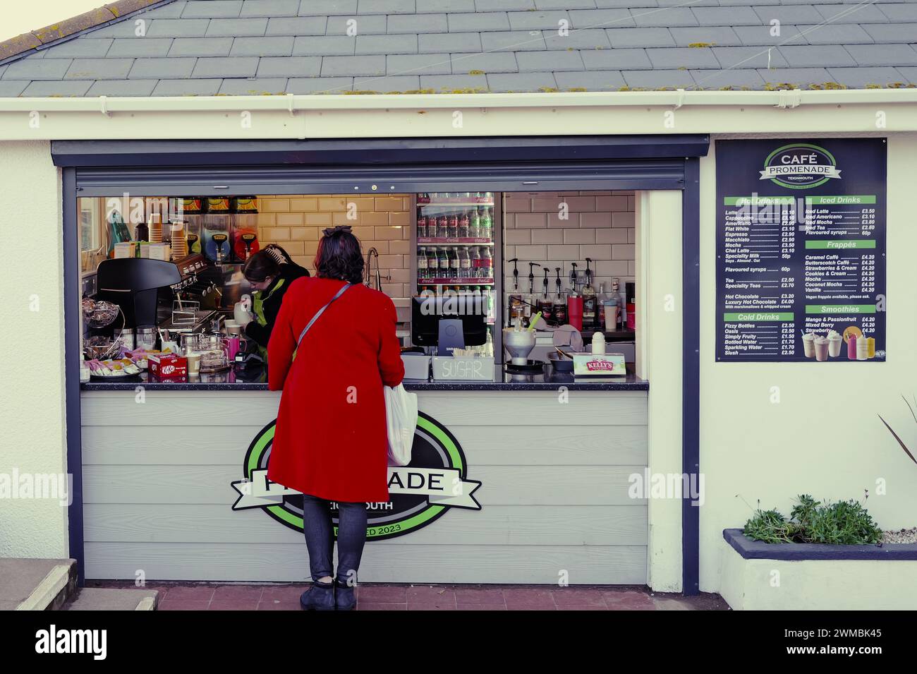 Woman in red coat being served at a food and drink kiosk on the promenade at Teignmouth, South Devon, sea front. Stock Photo