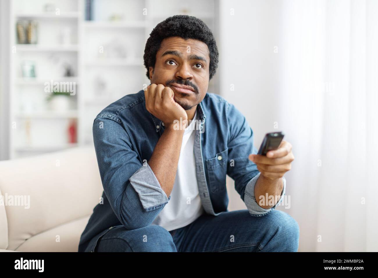 Portrait Of Bored Young Black Man Watching TV At Home Stock Photo