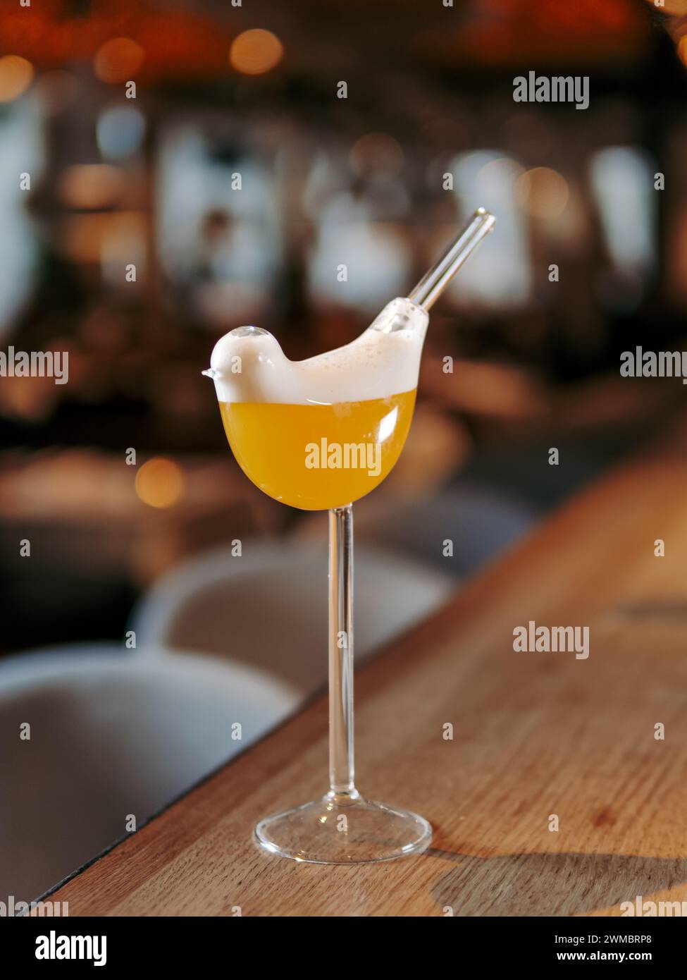 Tommy D Sour Cocktail in bird high stem cocktail glass on bar counter background with bokeh. Yellow alcohol Tommy Dee Sour cocktail made with whiskey, egg white, angostura, passion fruit syrup Stock Photo