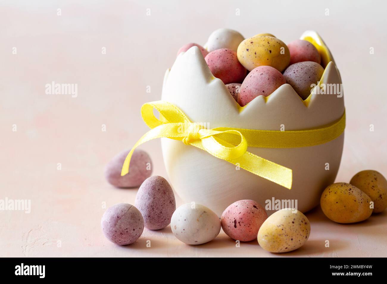 Colored chocolate easter eggs candy in eggshell shaped bowl on pink background, easter sweets, decoration Stock Photo