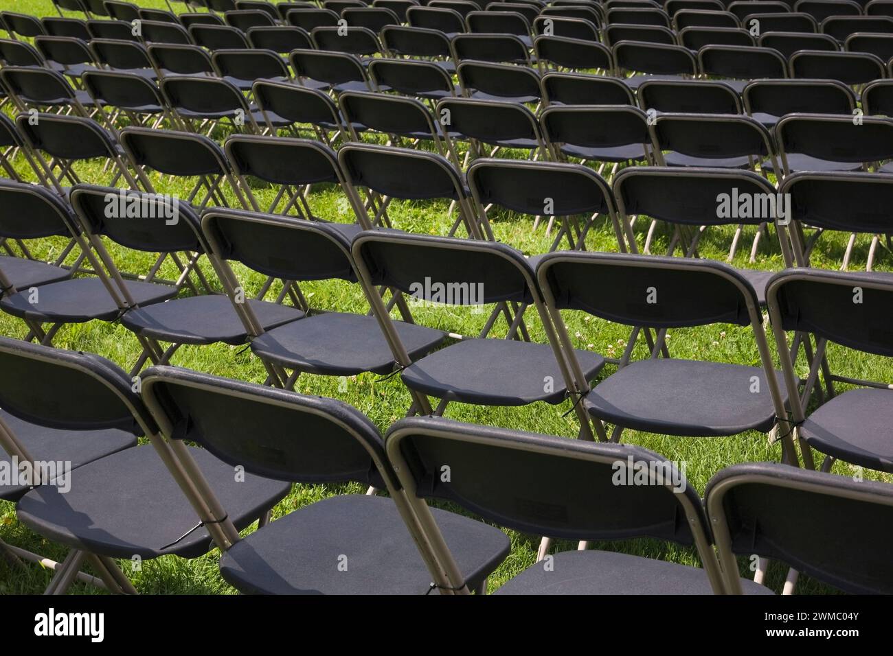 Rows of brown aluminium and black plastic folding sitting chairs on green grass set up for spectators attending an event in summer. Stock Photo