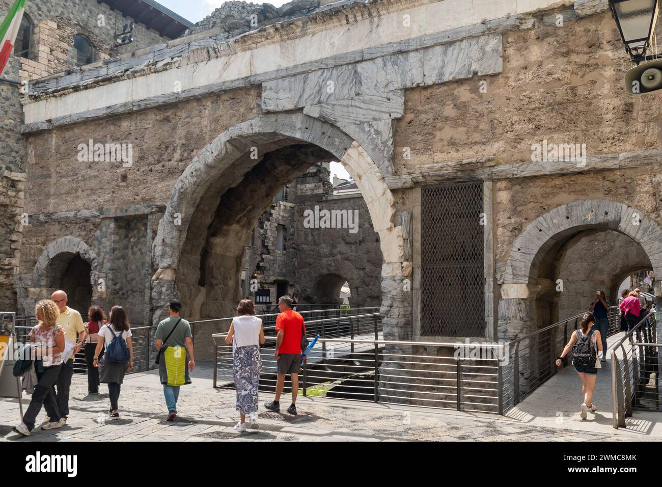 Tourists crossing the Pretoria Gate (25 BC), the Roman city gate, formed by two series of arches enclosing a parade ground, Aosta, Aosta Valley, Italy Stock Photo