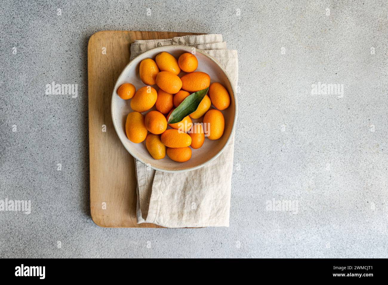 Overhead view of ripe kumquats in a bowl on a folded napkin and chopping board Stock Photo