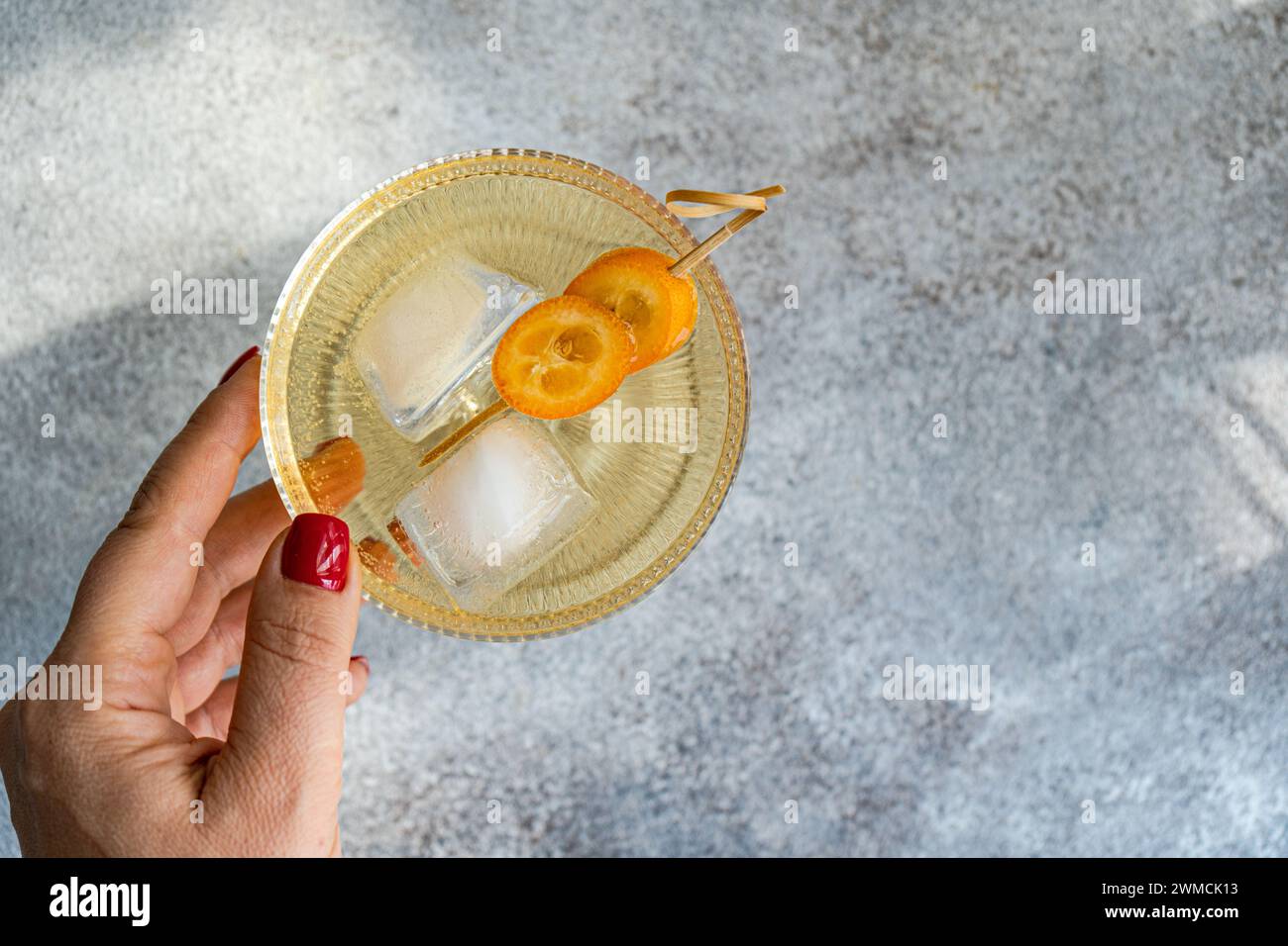 Overhead view of a woman reaching for a vodka tonic cocktail with kumquat garnish Stock Photo