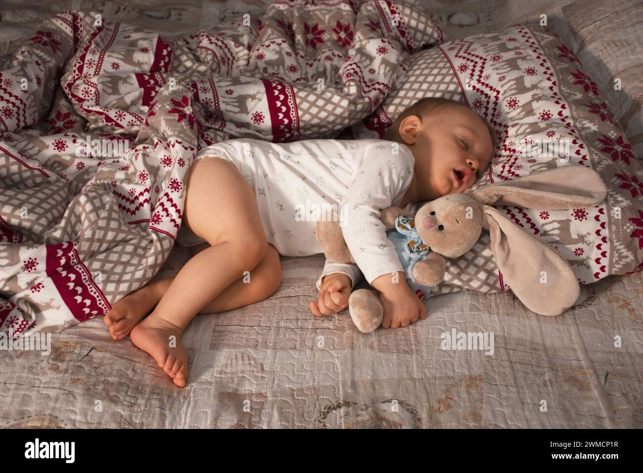baby sleeps sweetly, breathes through his mouth, hugging a soft toy bunny on a Christmas bed Stock Photo