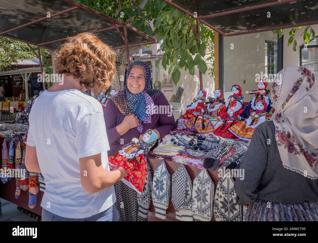 a tourist buys a handmade rag doll dressed in typical cappadocian clothes from a turkish woman who bargains with her with a smile, horizontal Stock Photo