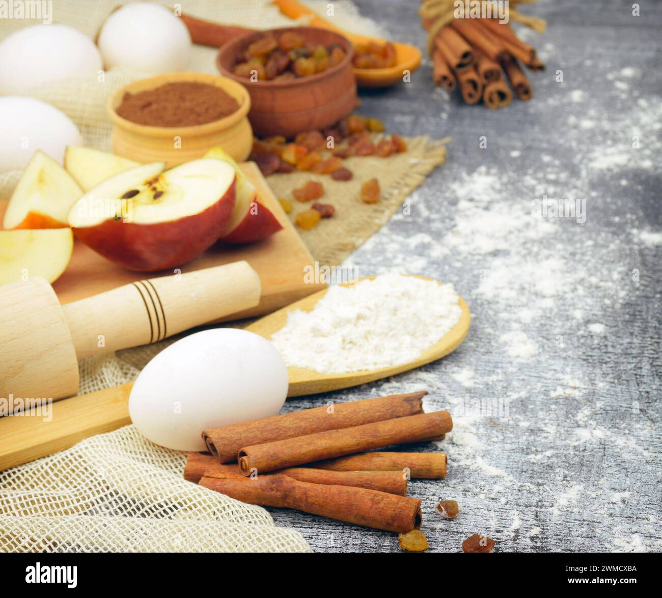 Ingredients for homemade pastries. Eggs, cinnamon, flour. apples, raisins, vanilla, and cookware. Concept: home cooking. Traditions. Cosiness. Stock Photo