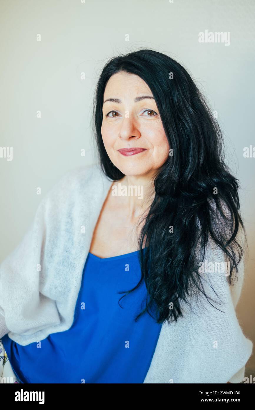 Confident middle-aged woman, radiant smile, blue attire, facing the onset of menopause. Perfect for content about women's midlife wellness, and emotio Stock Photo