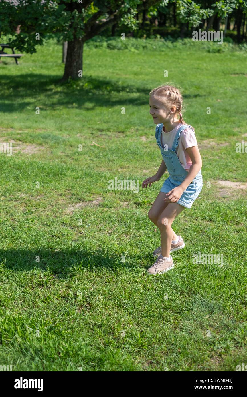 A little cute girl is running in a green grass and forest setting. Used for active and healthy time outside and insurances for kids safety. High quali Stock Photo