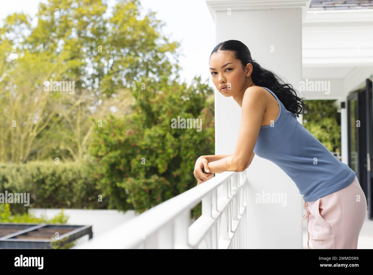 Young biracial woman leans on a balcony railing at home Stock Photo