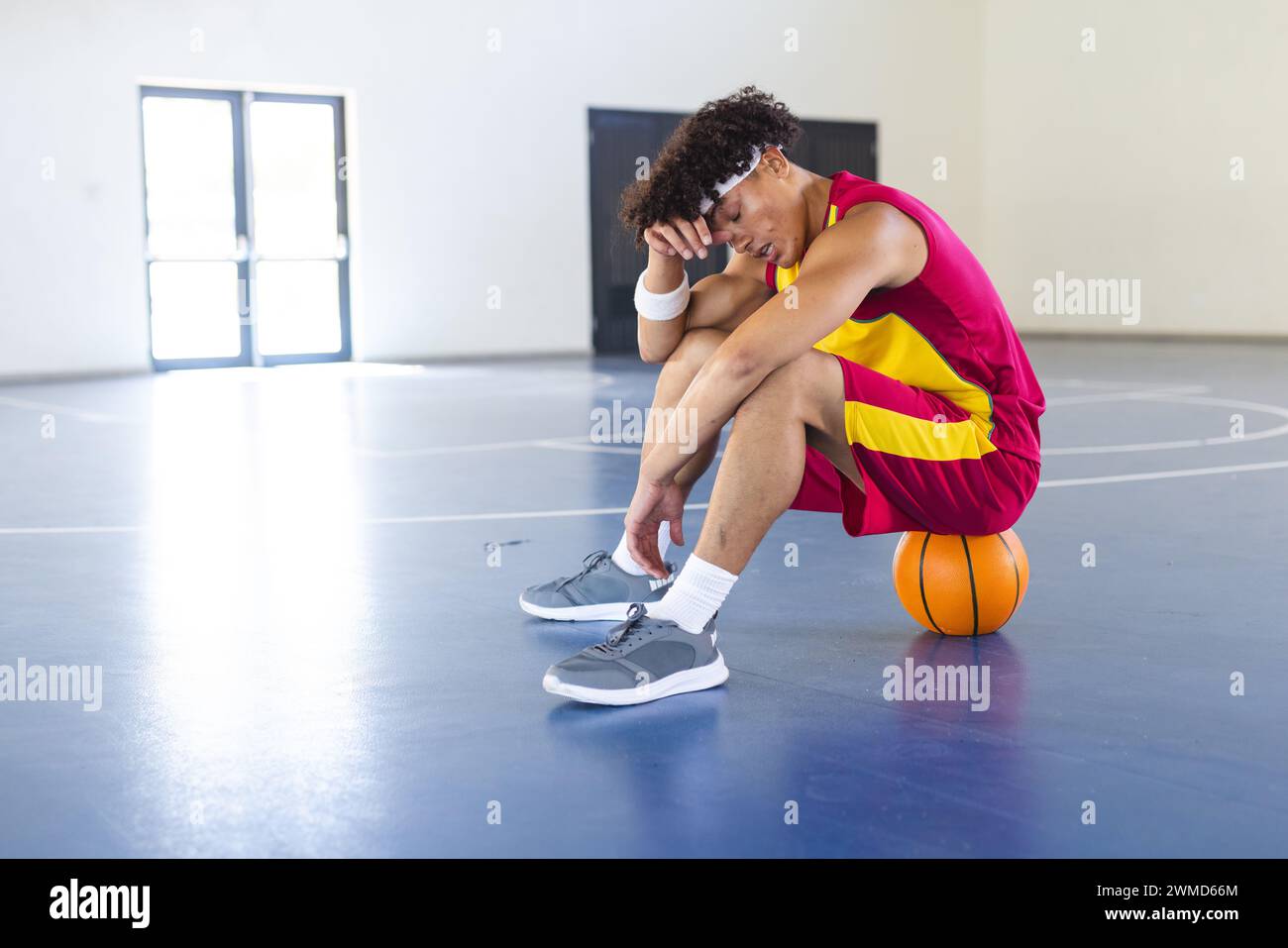 A young biracial man sits on a basketball, looking thoughtful Stock Photo