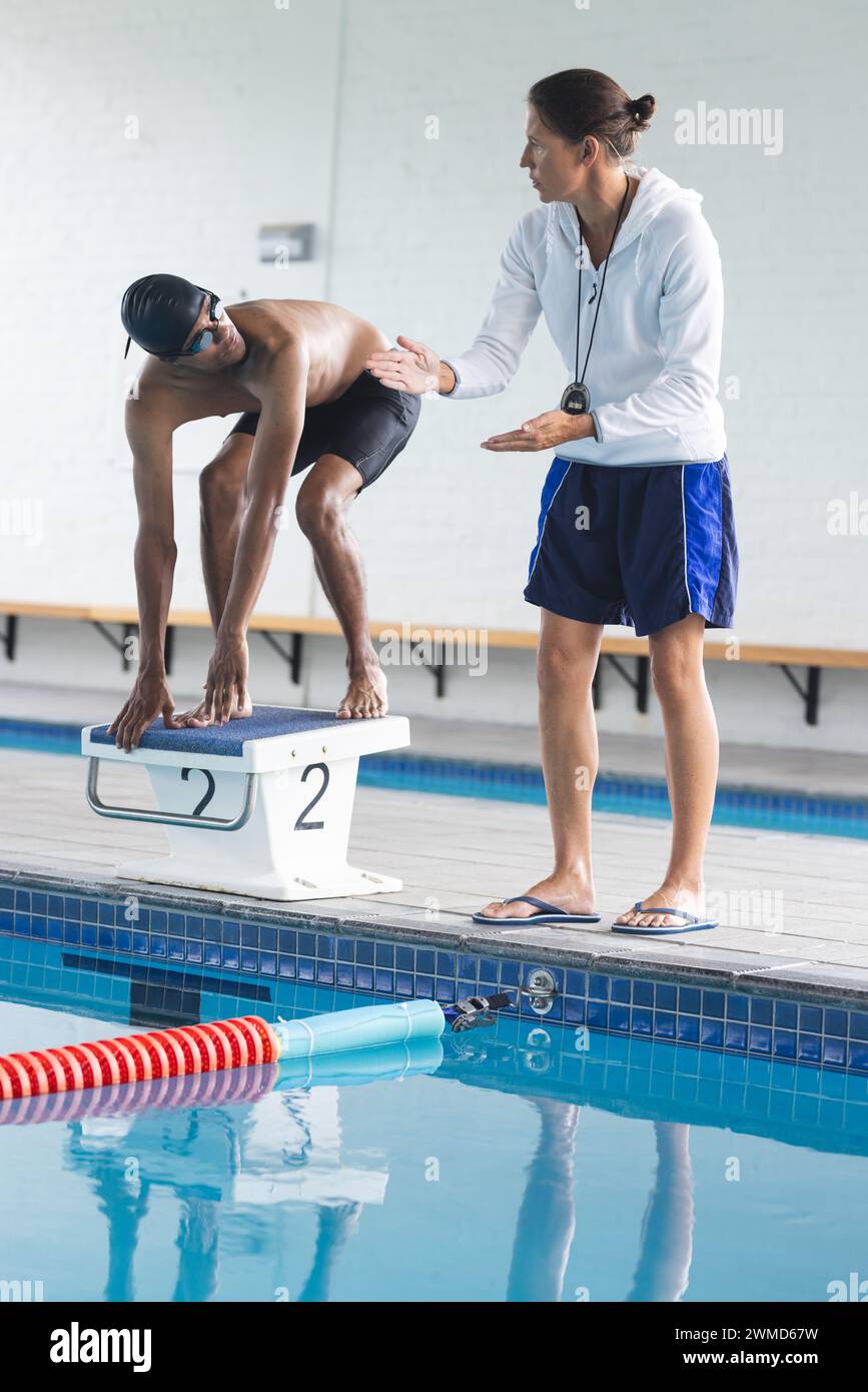 Coach instructs a young biracial male athlete swimmer by the poolside Stock Photo