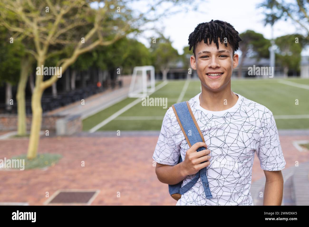 Teenage biracial boy smiles at high school's sports field with copy space Stock Photo