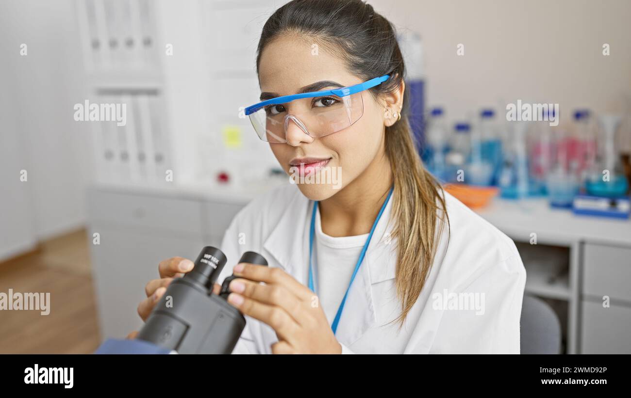 Hispanic woman scientist using microscope in laboratory setting, embodying expertise and healthcare professionalism. Stock Photo
