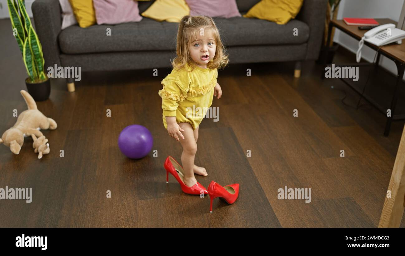 Cute blonde girl trying on red heels in a cluttered living room, depicting childhood innocence and playfulness at home. Stock Photo