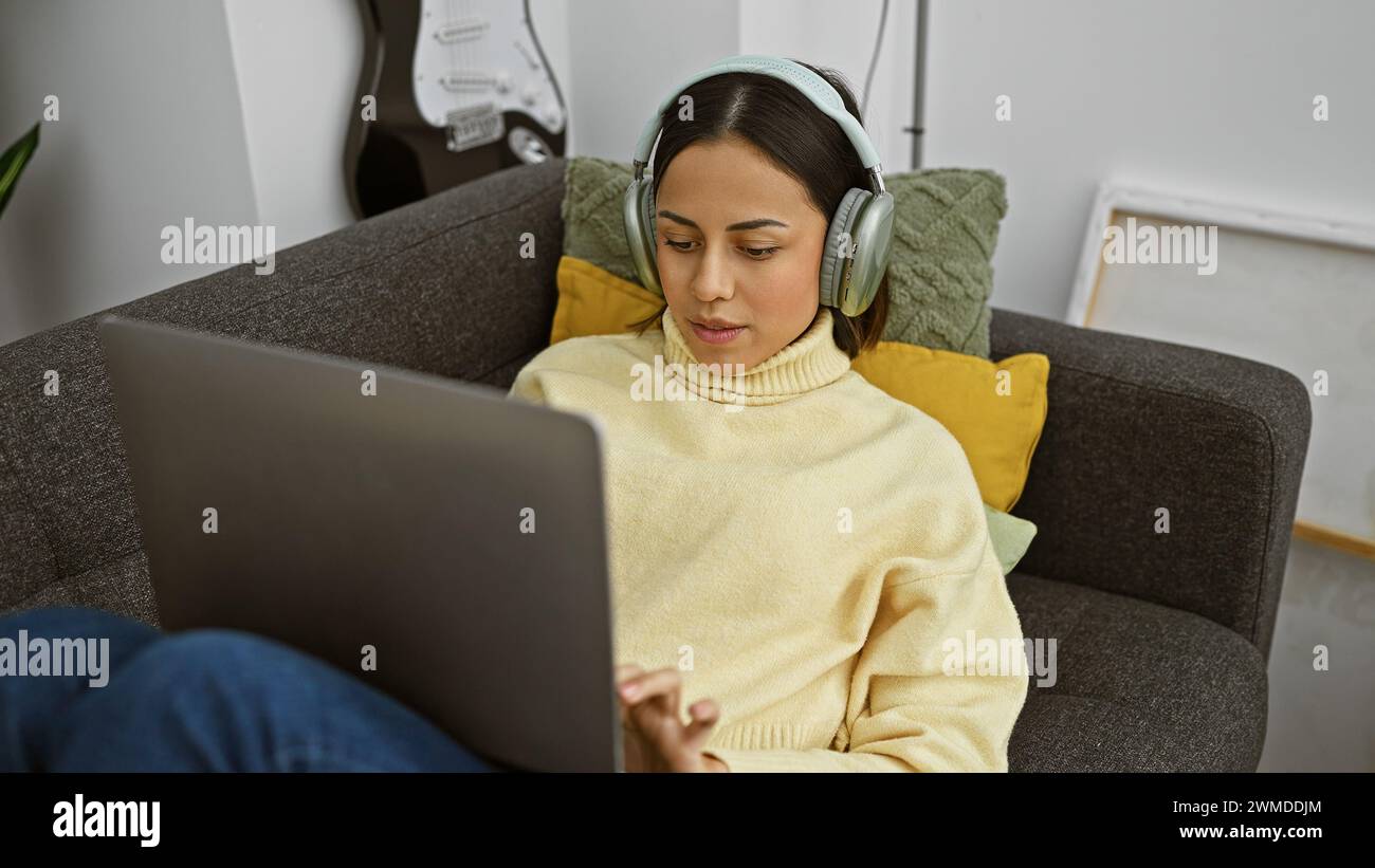 A focused hispanic woman wearing headphones uses a laptop while ...