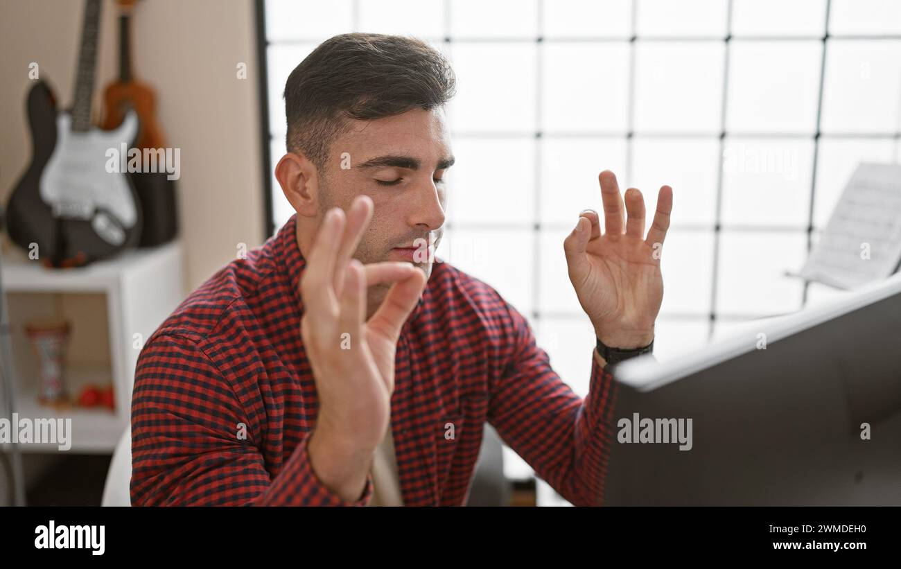 Young, handsome hispanic man, talented musician creating melody in the studio, finding balance and breath through yoga exercise. Stock Photo