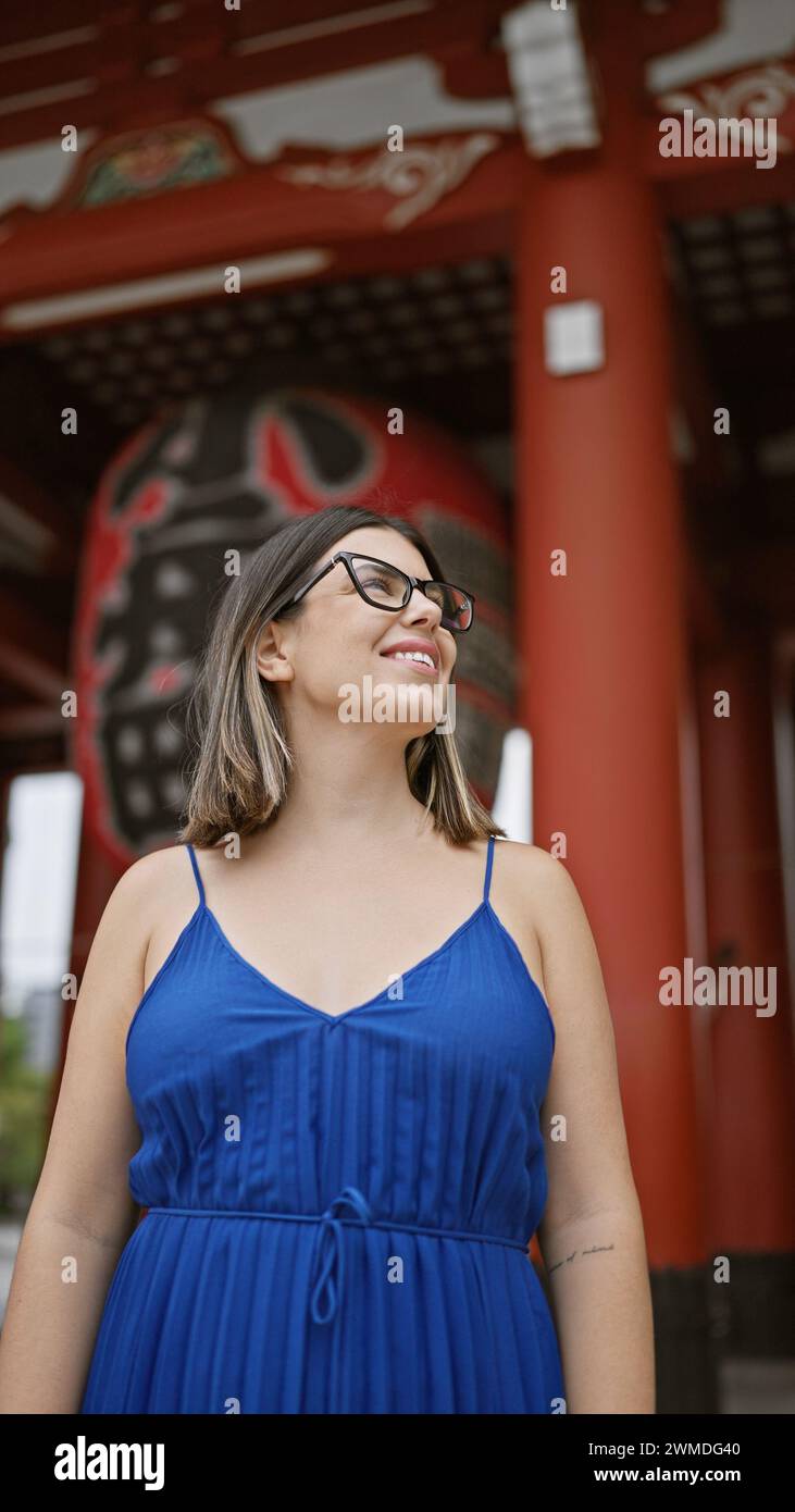 Cheerful, beautiful hispanic woman with glasses joyfully exploring and admiring the majestic senso-ji temple as she casually strolls, looking around w Stock Photo
