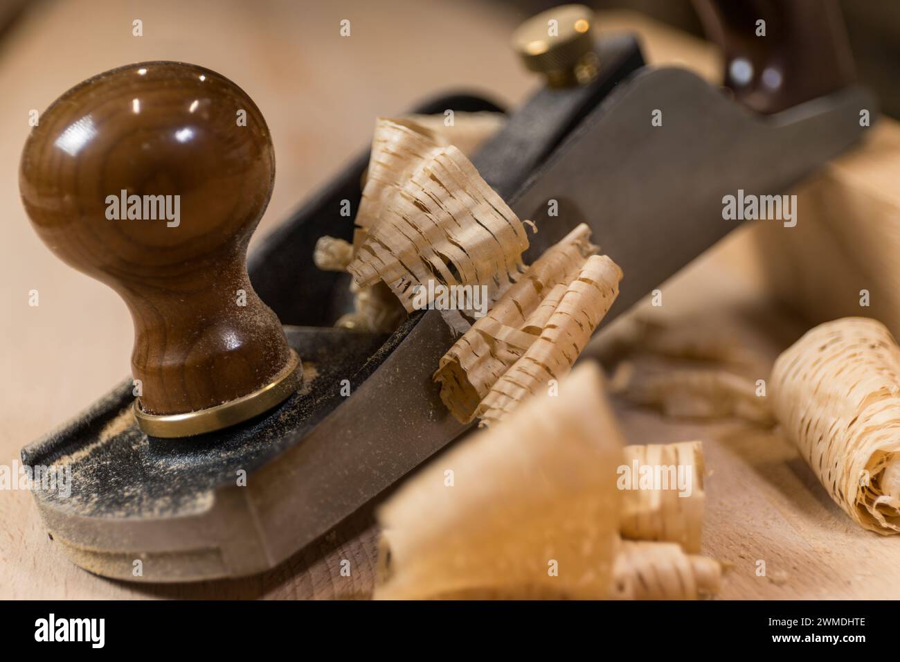 Horizontal photo close-up of an antique hand plane on a wooden surface, surrounded by delicate wood shavings, highlighting fine craftsmanship. Busines Stock Photo