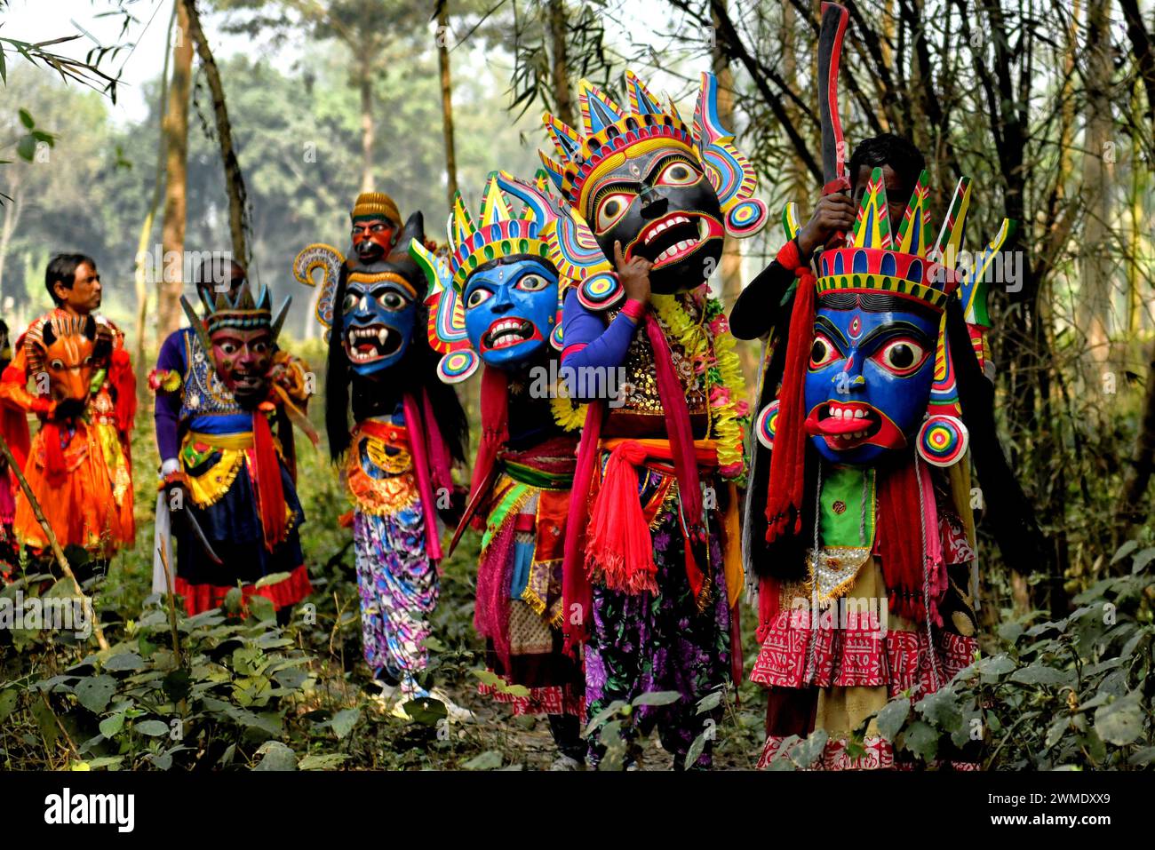 Masked dancers of Gomira dance troupe wait at a bamboo field during their performance at a village near Raiganj. Gomira is a masked dance form. The word ‘Gomira' has been derived from the colloquial form of the word ‘Gram-Chandi' or the female deity who is the protective force of the village. The exact origin of the dance form is not traceable and the knowledge has been lost over time. Gomira dance is a rural dance form mainly practiced in the Dinajpur district of West Bengal. The Gomira dances are organized to appease the deity to usher in the 'good forces' and drive out the 'evil forces'. It Stock Photo