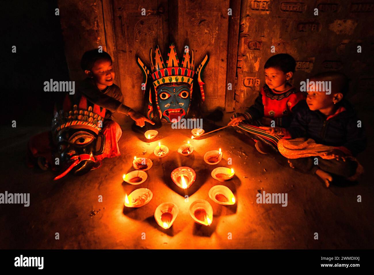 Children light Diyas (Soil made Lamp) in front of the face masks at a village near Raiganj. Gomira is a masked dance form. The word ‘Gomira' has been derived from the colloquial form of the word ‘Gram-Chandi' or the female deity who is the protective force of the village. The exact origin of the dance form is not traceable and the knowledge has been lost over time. Gomira dance is a rural dance form mainly practiced in the Dinajpur district of West Bengal. The Gomira dances are organized to appease the deity to usher in the 'good forces' and drive out the 'evil forces'. It is usually organised Stock Photo