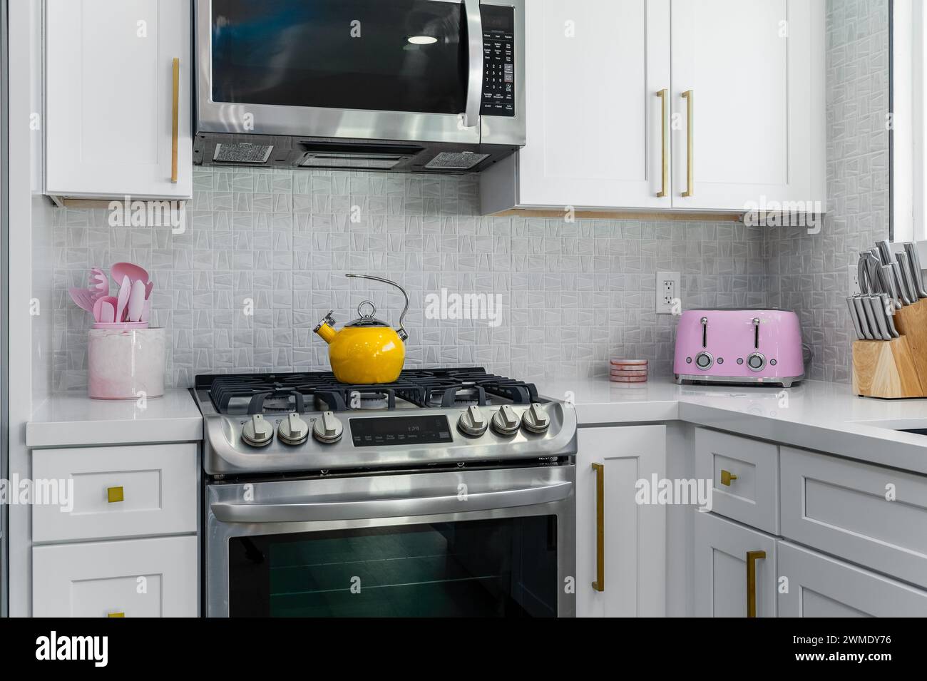 Bright white kitchen with stainless stove, oven, and microwave with colorful decor Stock Photo