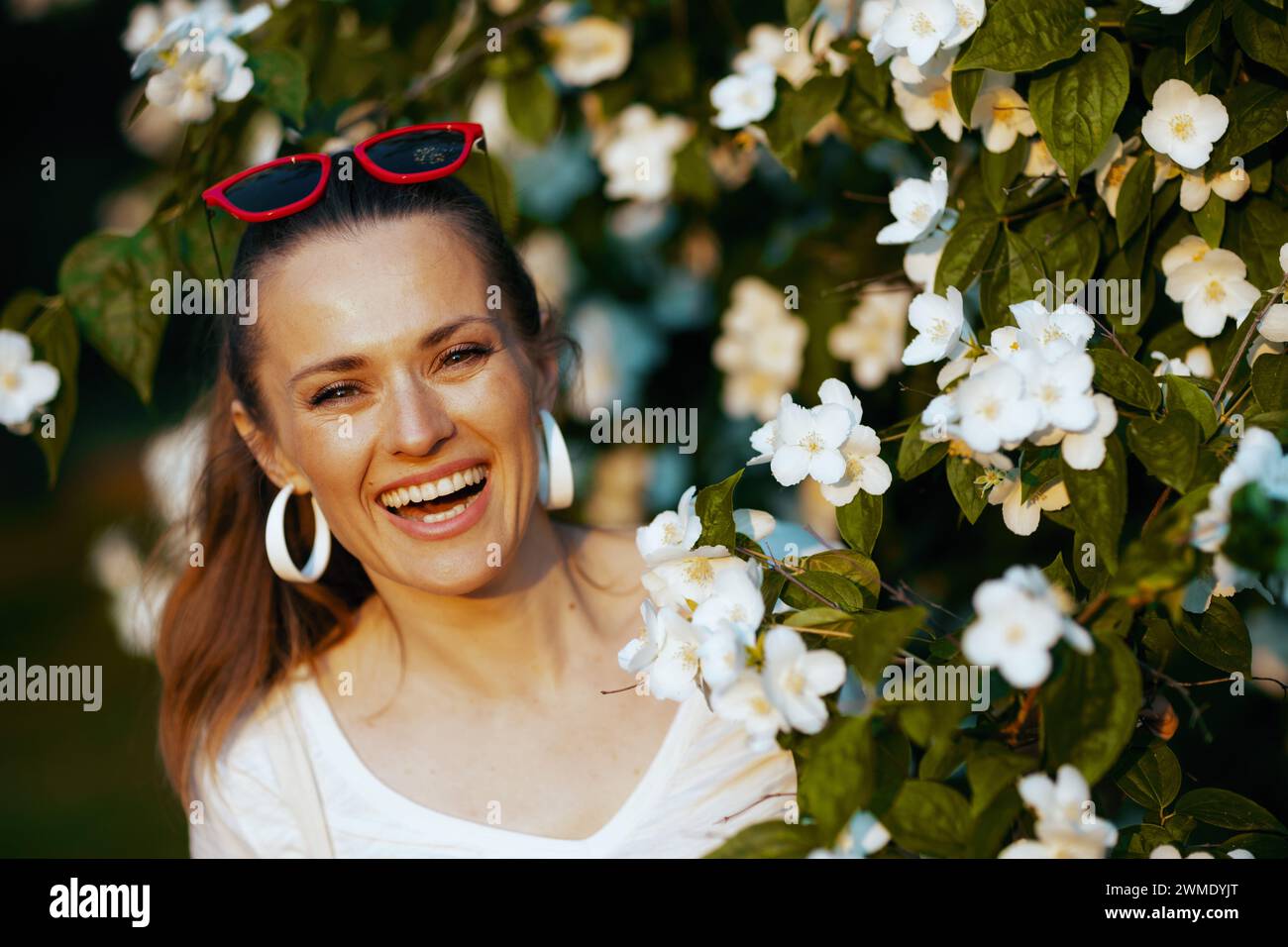 Summer time. Portrait of happy elegant female in white shirt near flowering tree. Stock Photo