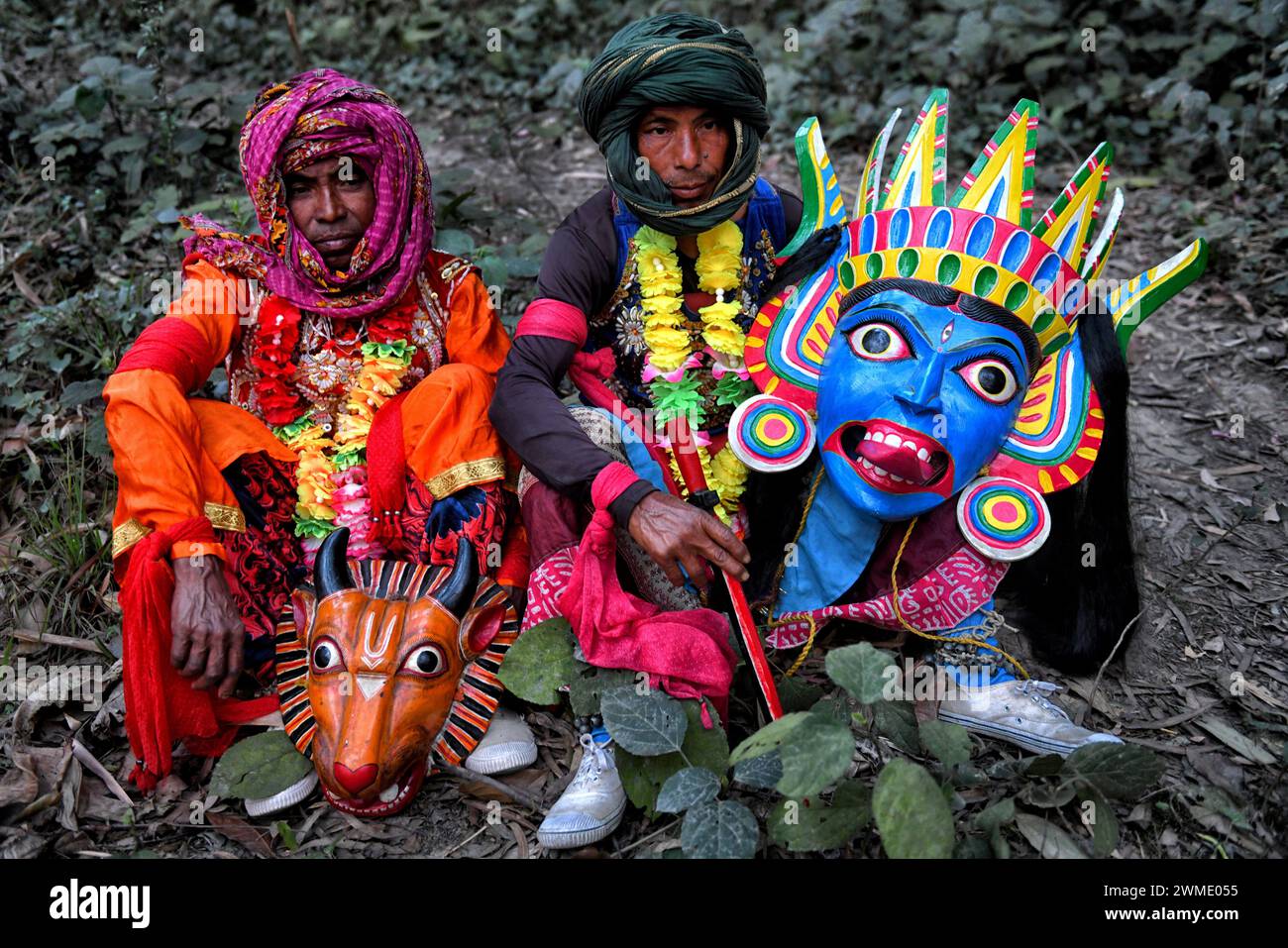 Two Masked dancers of Gomira dance troupe take break in between their performance at a village near Raiganj. Gomira is a masked dance form. The word ‘Gomira' has been derived from the colloquial form of the word ‘Gram-Chandi' or the female deity who is the protective force of the village. The exact origin of the dance form is not traceable and the knowledge has been lost over time. Gomira dance is a rural dance form mainly practiced in the Dinajpur district of West Bengal. The Gomira dances are organized to appease the deity to usher in the 'good forces' and drive out the 'evil forces'. It is Stock Photo