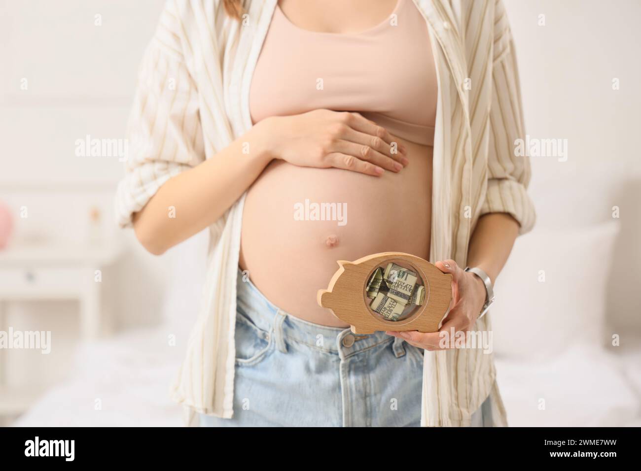 Young pregnant woman with piggy bank in bedroom, closeup. Maternal Benefit concept Stock Photo