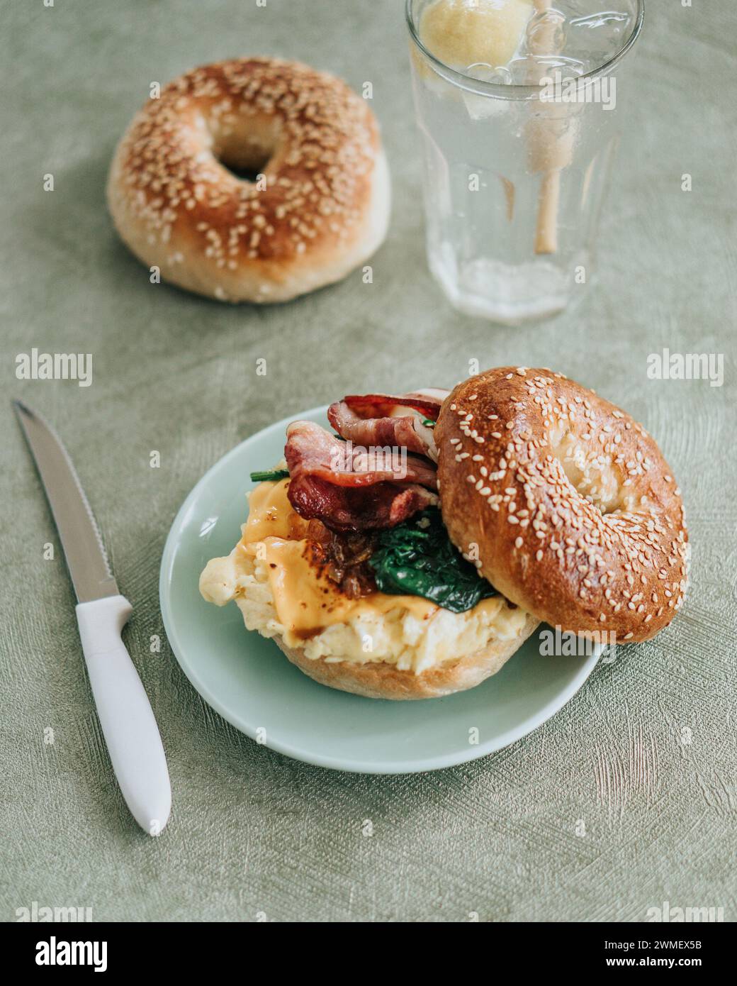 A toasted bagel breakfast sandwich with eggs, spinach, and bacon on a green plate Stock Photo