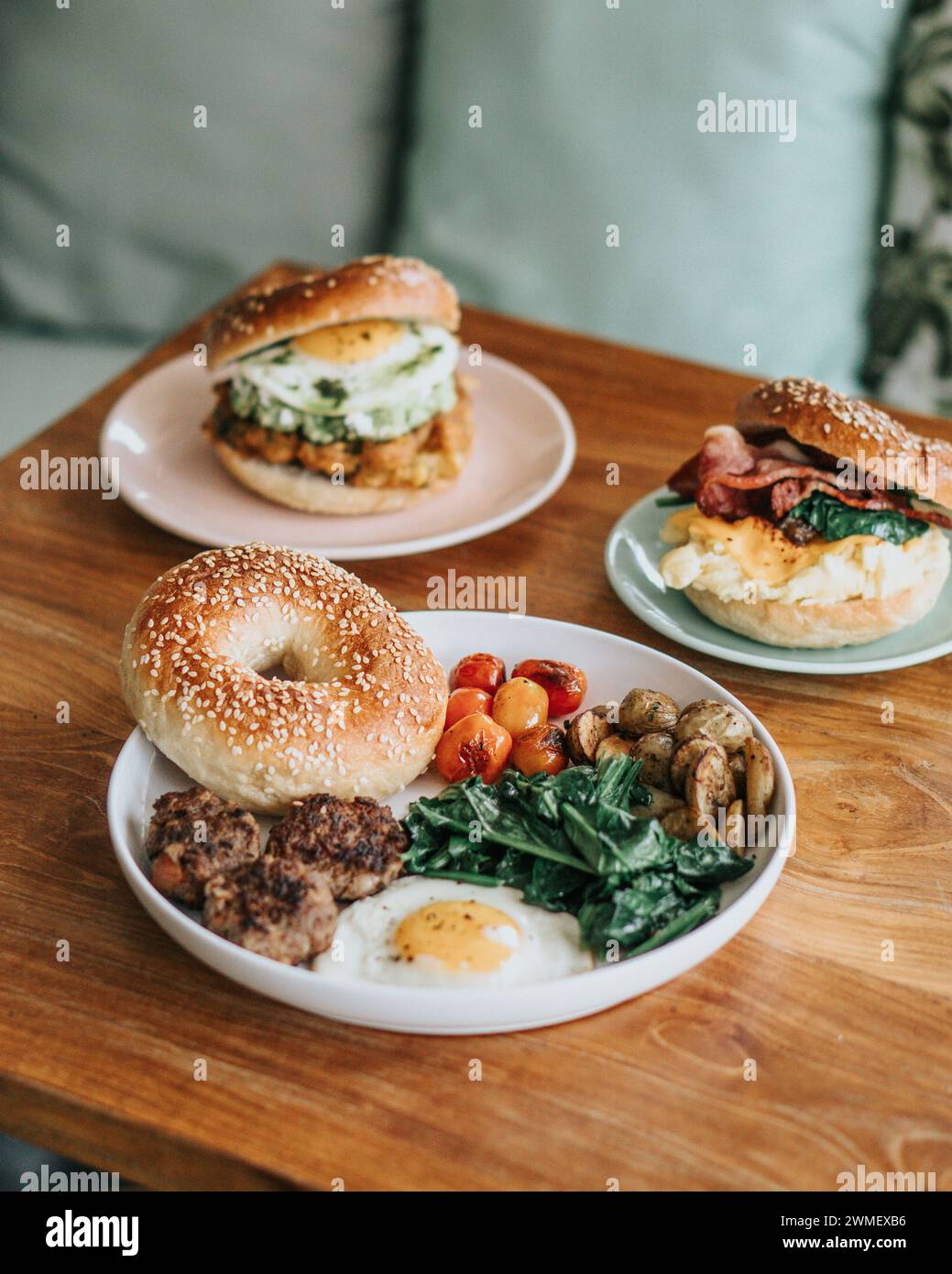 Three plates of food on a wooden table is a breakfast sandwich on a toasted bagel, salad, and burrito Stock Photo
