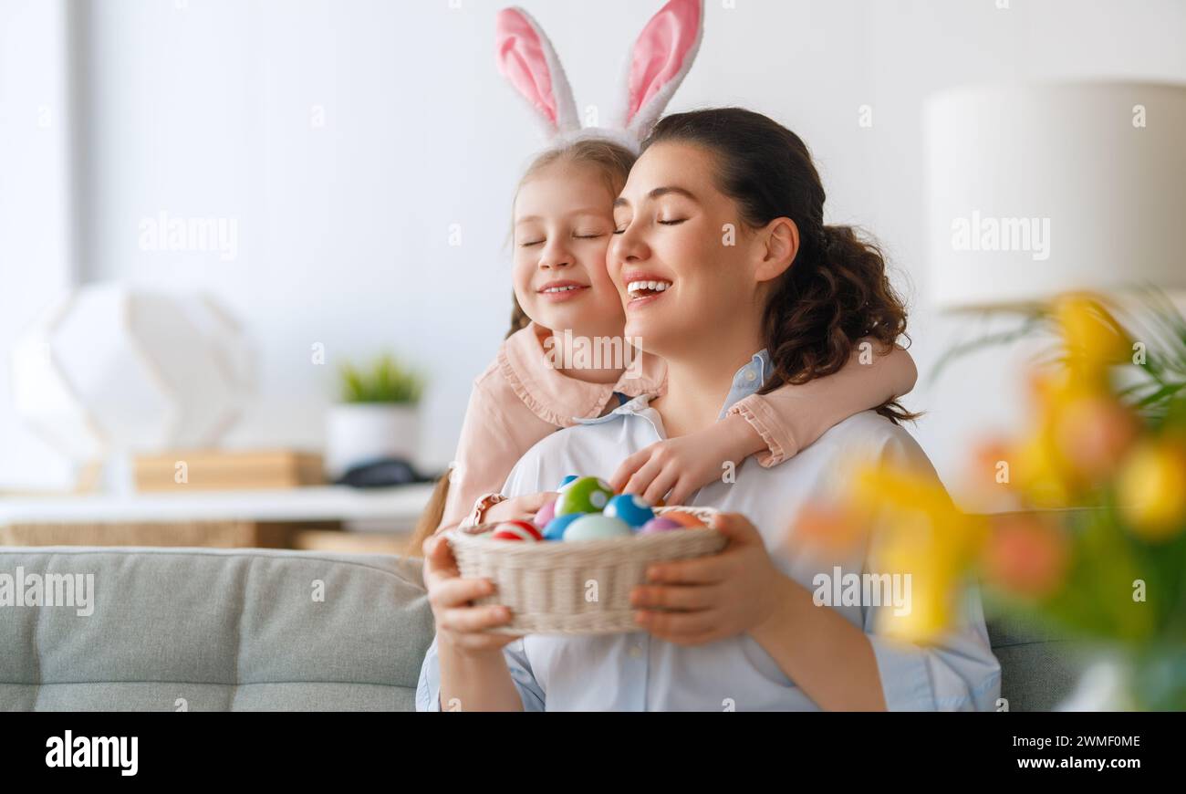 Happy holiday! Mother and her daughter with painting eggs. Family celebrating Easter. Cute little child girl is wearing bunny ears. Stock Photo