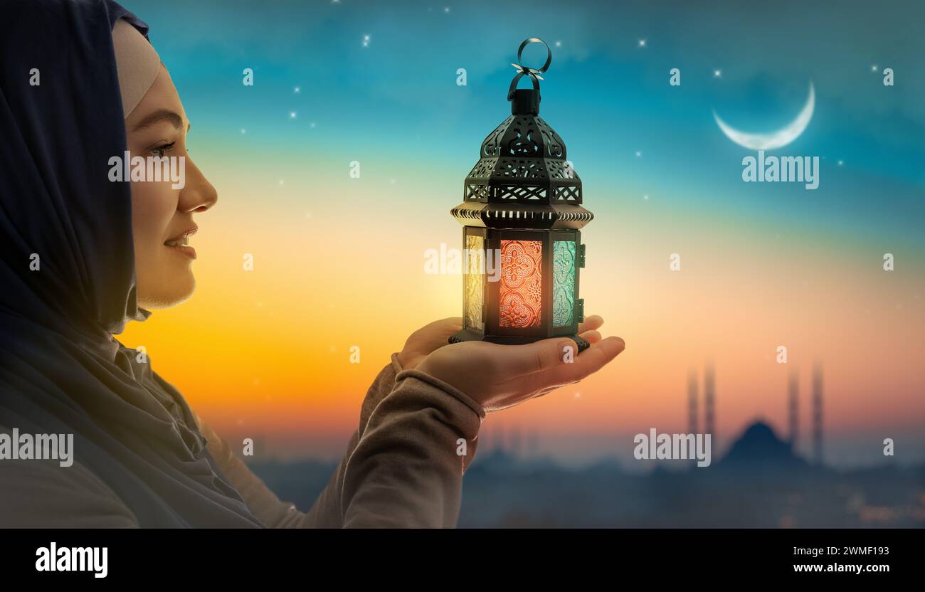 Woman is holding Ornamental Arabic lantern with burning candle glowing at night mosque background. Festive greeting card, invitation for Muslim holy m Stock Photo
