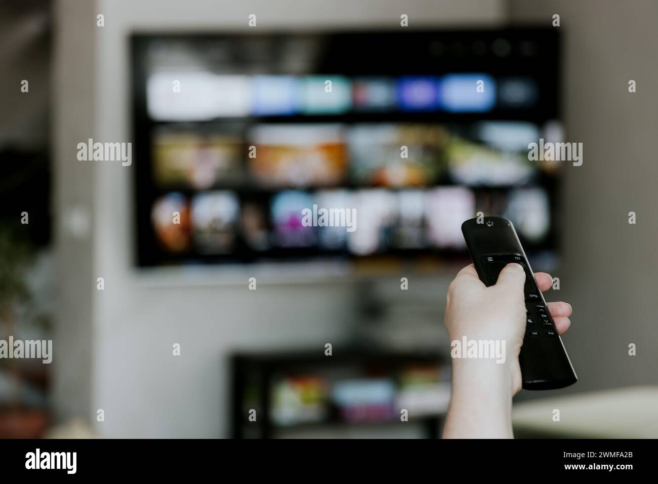 Hand holding remote control pointing to TV. Person watching smart ...