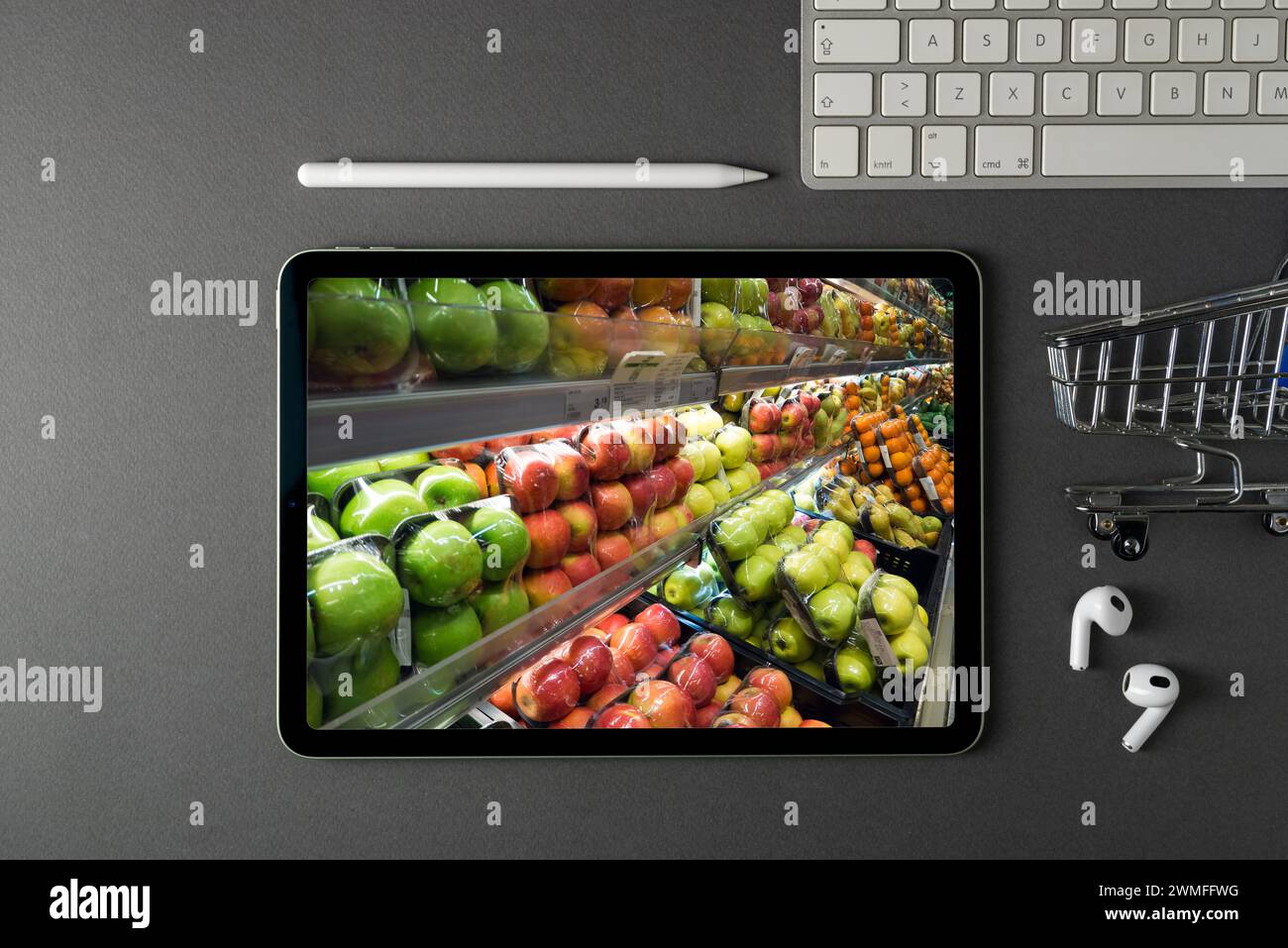 Tablet with grocery section on screen on dark gray office desk. There is a grocery cart and a keyboard next to him Stock Photo