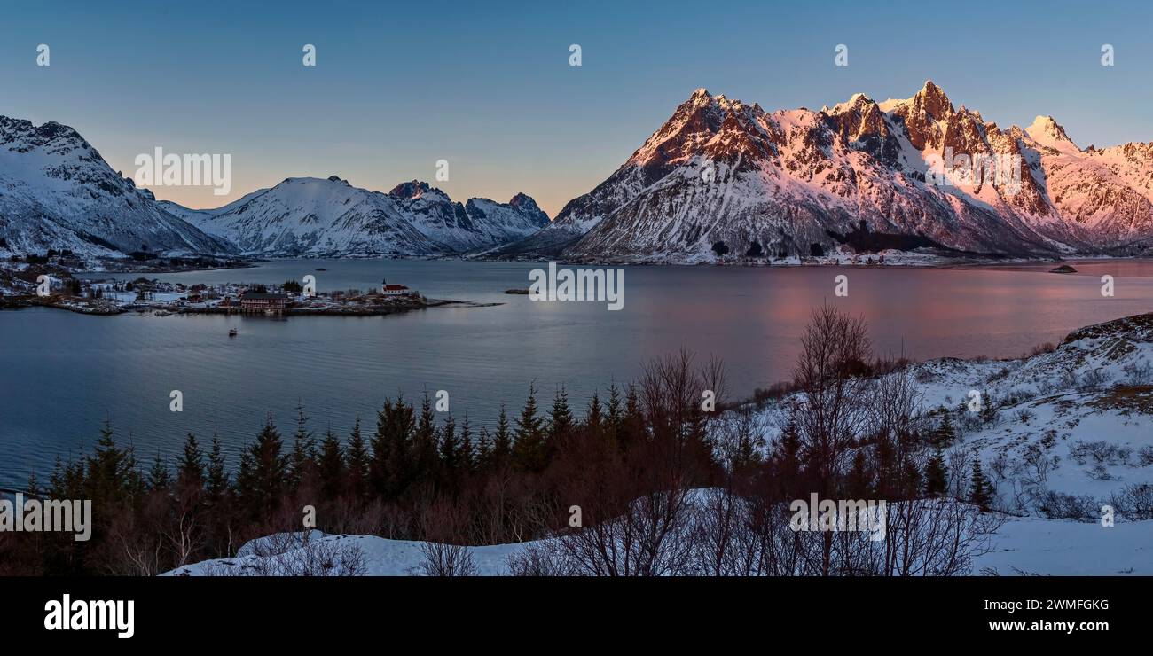Die untergehende Sonne beleuchtet schneebedeckte Berge an einem ruhigen See, Lofoten Stock Photo