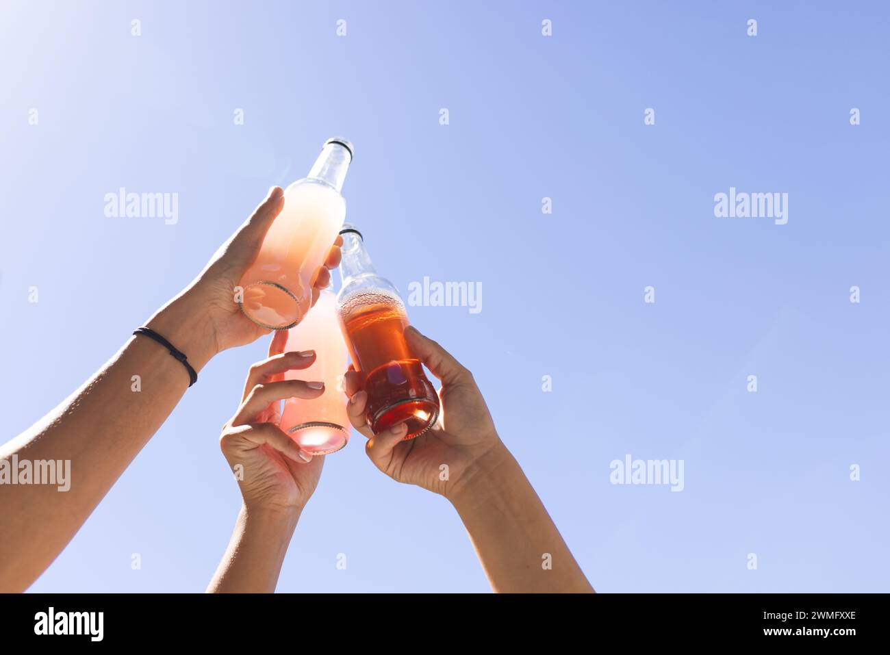 Hands clinking bottles against a clear blue sky Stock Photo