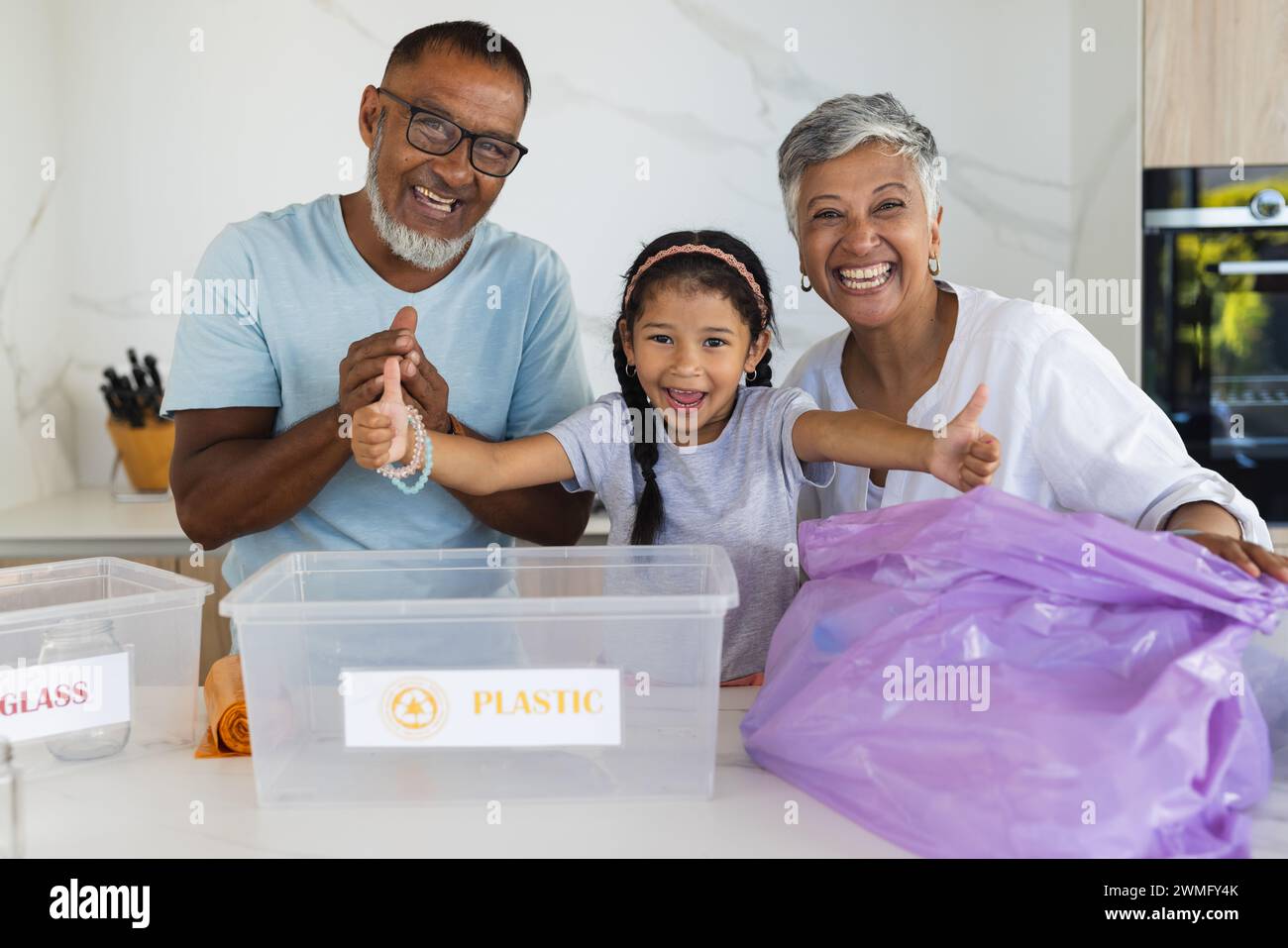 Biracial grandparents and granddaughter sort recycling in the kitchen Stock Photo