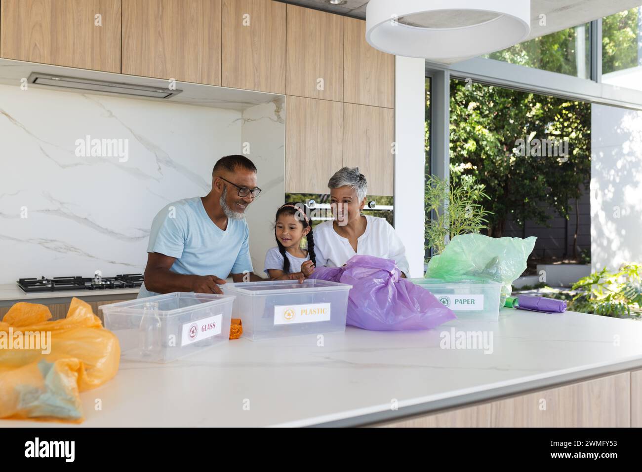 Biracial grandparents and granddaughter sort recycling in a bright kitchen, with copy space Stock Photo