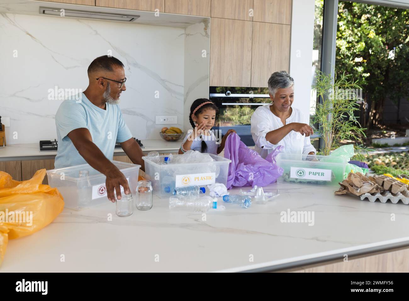 Biracial grandparents and granddaughter sort recycling in a bright kitchen Stock Photo
